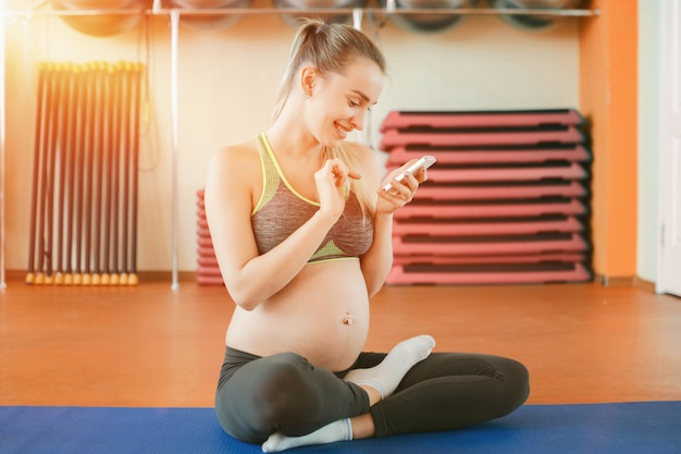 Giovane donna incinta che per mezzo dello smartphone alla palestra