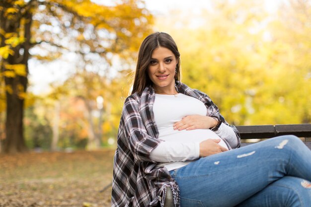 Giovane donna incinta che si siede nella sosta di autunno