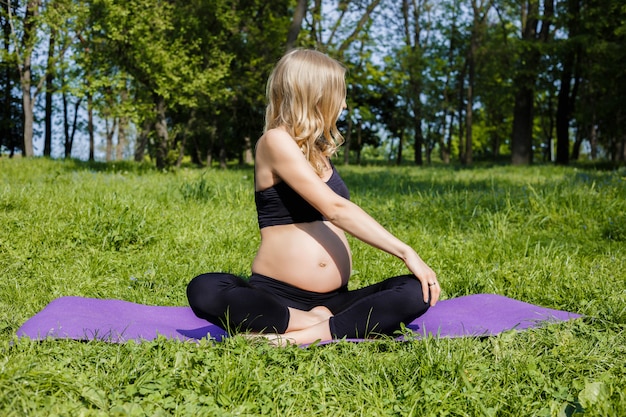 giovane donna incinta che si siede sull'erba che fa yoga nel giorno di estate