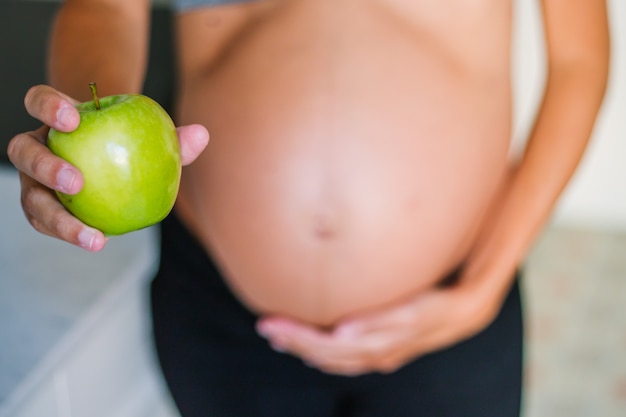 Giovane donna incinta che tiene e che mostra una mela a casa