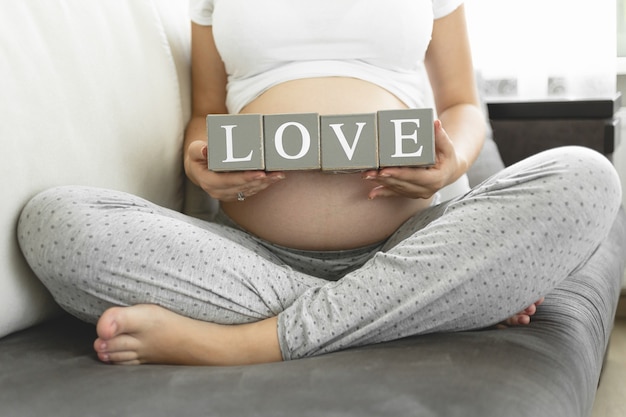 Giovane donna incinta che tiene i blocchi con la lettera che fa la parola Love