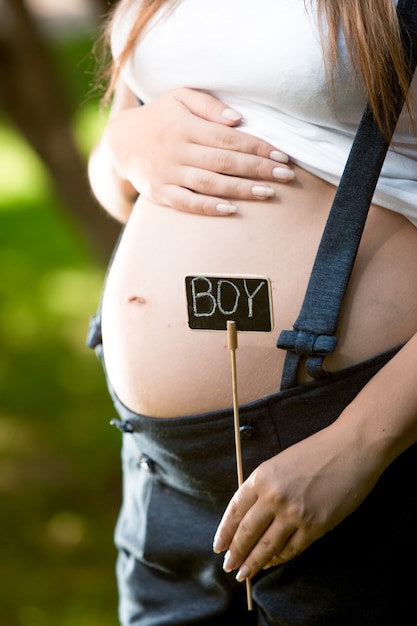 Giovane donna incinta che tiene piccola lavagna all'addome con la parola "ragazzo"