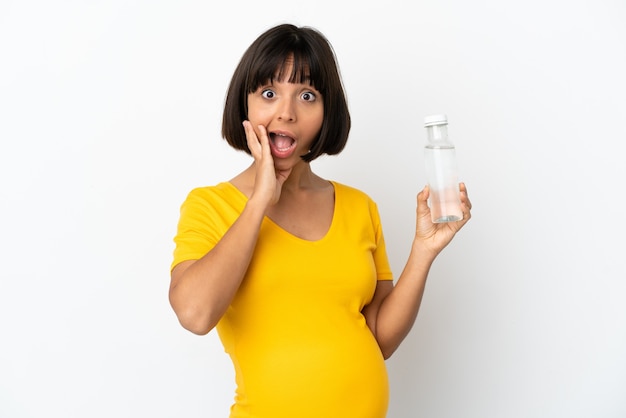 Giovane donna incinta che tiene una bottiglia d'acqua isolata su sfondo bianco con espressione facciale sorpresa e scioccata shock