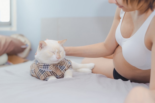Giovane donna incinta con il gatto sveglio dell'animale domestico sul letto a casa