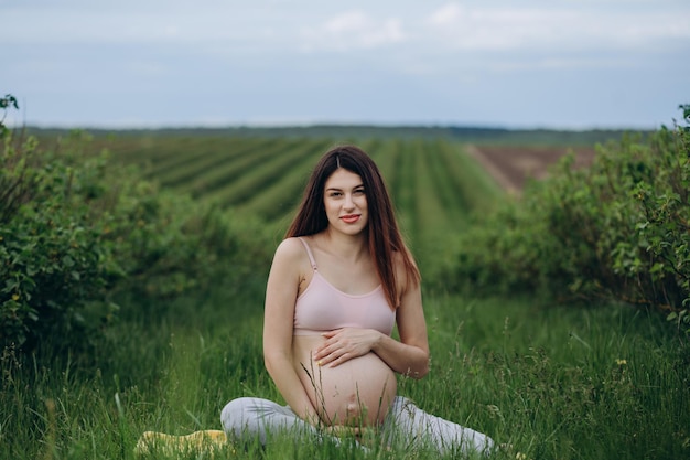 Giovane donna incinta con reggiseno sportivo che fa yoga in natura all'aperto