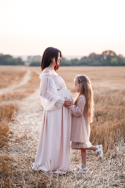 Giovane donna incinta con sua figlia famiglia felice che si abbraccia su un campo d'oro in campagna Relazioni familiari