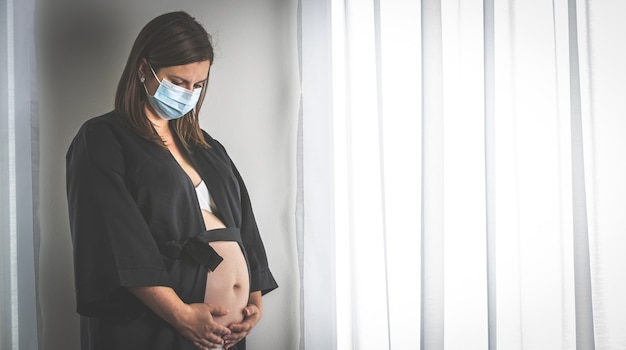 Giovane donna incinta con una maschera medica durante la pandemia di coronavirus, gravidanza durante il covid-2019