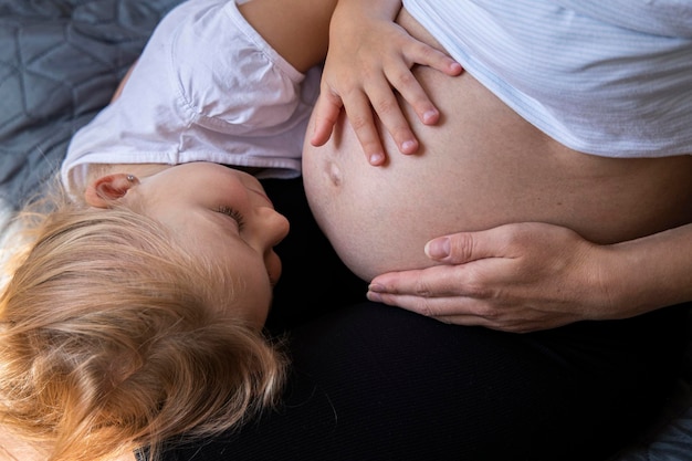 Giovane donna incinta e figlia che ascoltano il bambino che tiene il ventre Vista dall'alto distesa piatta