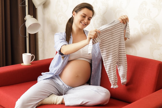 Giovane donna incinta guardando la tuta per il suo futuro bambino