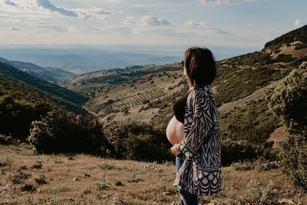 Giovane donna incinta in natura con sfondo di montagne e nuvole