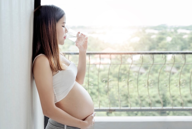 Giovane donna incinta in piedi e acqua potabile