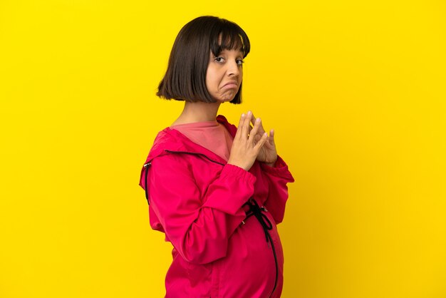 Giovane donna incinta su sfondo giallo isolato che trama qualcosa