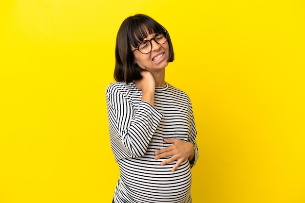 Giovane donna incinta su sfondo giallo isolato con mal di collo