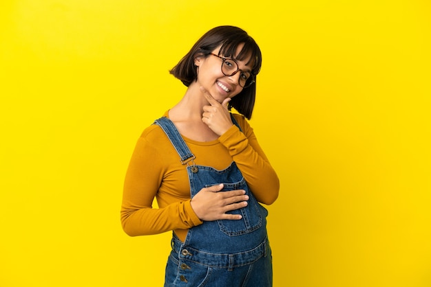 Giovane donna incinta su sfondo giallo isolato felice e sorridente