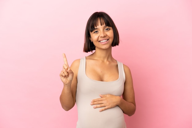 Giovane donna incinta su sfondo rosa isolato che mostra e alza un dito in segno del meglio