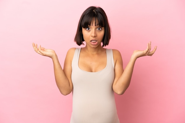 Giovane donna incinta su sfondo rosa isolato con espressione facciale scioccata