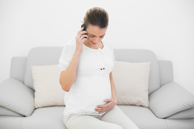 Giovane donna incinta telefonando mentre si tiene la sua pancia e guardando