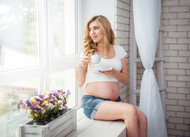 Giovane donna incinta vicino ad una finestra.