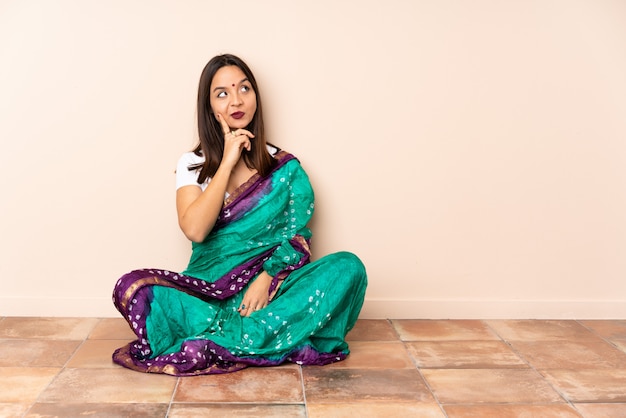 Giovane donna indiana che si siede sul pavimento che ha dubbi mentre osserva in su