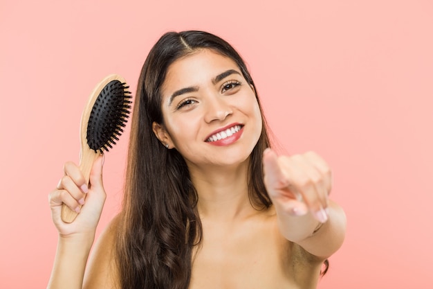 Giovane donna indiana che tiene i sorrisi allegri di una spazzola per i capelli che indicano la parte anteriore.