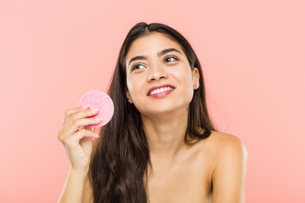 Giovane donna indiana che tiene sorridere sorridente del disco di cura di pelle facciale sicuro con le armi attraversate.