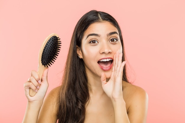 Giovane donna indiana che tiene una spazzola per capelli che grida eccitato alla parte anteriore.