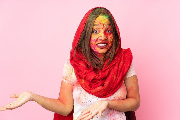 Giovane donna indiana con le polveri colorate di holi sul suo fronte isolato sulla parete rosa con l'espressione di sorpresa mentre osservando lato