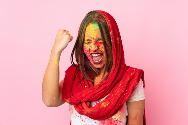 Giovane donna indiana con le polveri colorate di holi sul suo viso sulla parete rosa che celebra una vittoria