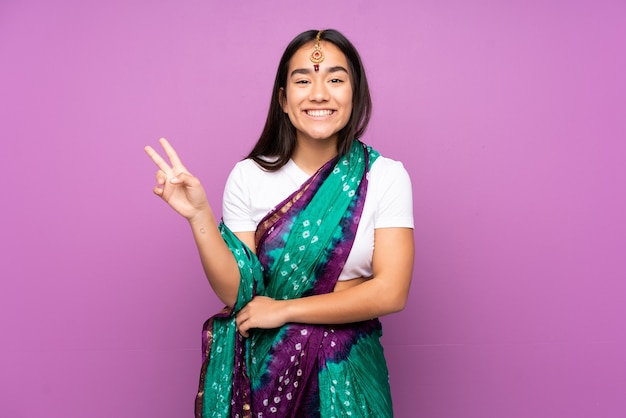 Giovane donna indiana con sari isolato su sorridente e mostrando il segno di vittoria
