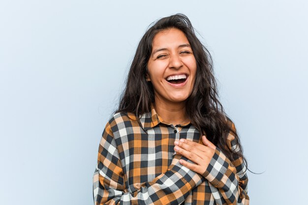 Giovane donna indiana fresca che ride tenendo le mani sul cuore, concetto di felicità.