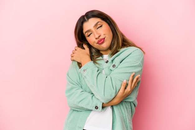 Giovane donna indiana isolata su sfondo rosa abbracci, sorridendo spensierata e felice.