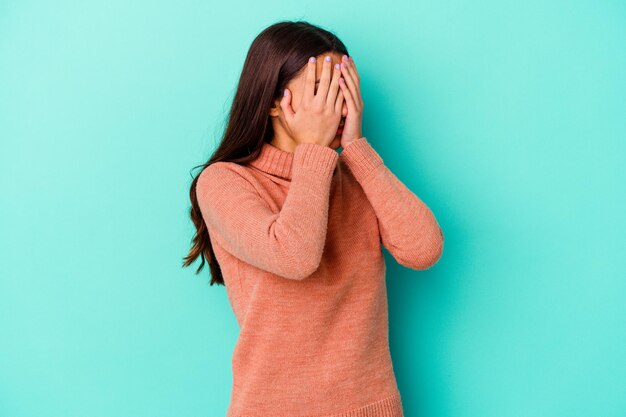 Giovane donna indiana isolata sugli occhi che coprono paura blu con le mani.