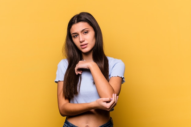 Giovane donna indiana isolata sul muro giallo massaggiando il gomito, che soffre dopo un brutto movimento.