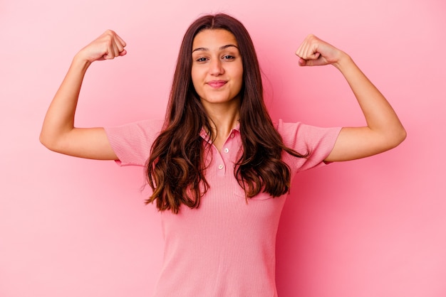 Giovane donna indiana isolata sul rosa che mostra il gesto di forza con le braccia, simbolo del potere femminile