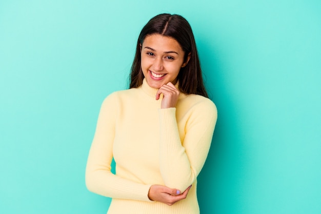 Giovane donna indiana isolata sul sorriso blu felice e fiducioso, toccando il mento con la mano.