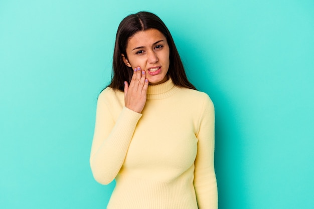 Giovane donna indiana isolata sulla parete blu che ha un forte dolore ai denti, dolore molare.