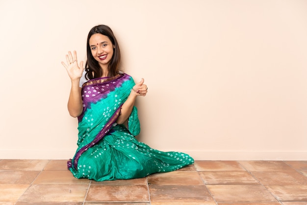 Giovane donna indiana seduta sul pavimento a contare sei con le dita