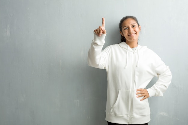 Giovane donna indiana sportiva contro una parete della palestra che mostra numero uno