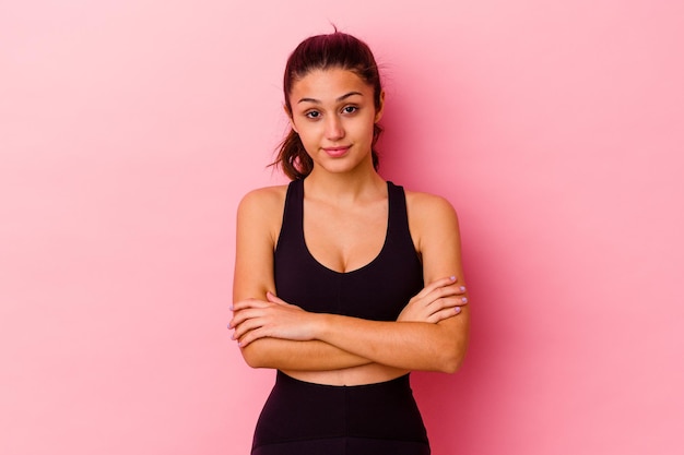 Giovane donna indiana sportiva isolata sul rosa che si sente sicura di sé, incrociando le braccia con determinazione.