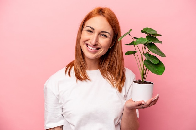 Giovane donna indoeuropea in possesso di un impianto isolato su sfondo rosa Giovane donna indoeuropea in possesso di un impianto isolato su sfondo rosa felice sorridente e allegro