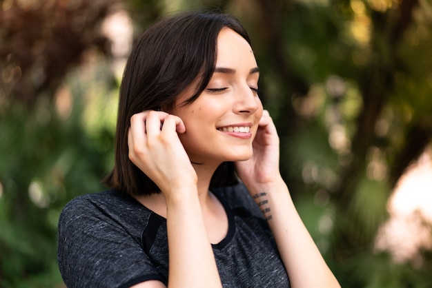 Giovane donna indoeuropea sport ascoltando musica all'aperto in un parco