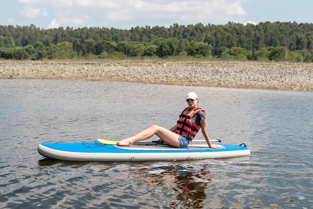 giovane donna indossa un giubbotto di salvataggio paddle boarding su un bel lago in estate caldo giorno stile di vita attivo sport e relax