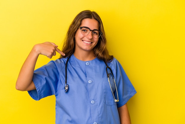 Giovane donna infermiera isolata su sfondo giallo persona che indica a mano uno spazio per la copia di una camicia, orgogliosa e sicura di sé