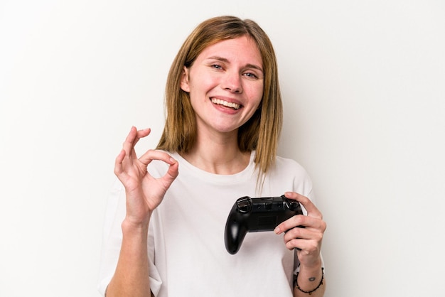 Giovane donna inglese che gioca con un controller per videogiochi isolato su sfondo bianco allegro e sicuro di sé che mostra un gesto ok