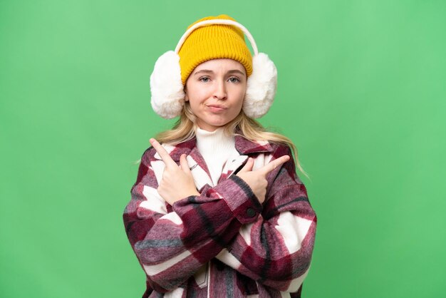 Giovane donna inglese che indossa manicotti invernali su sfondo isolato che punta ai laterali che hanno dubbi
