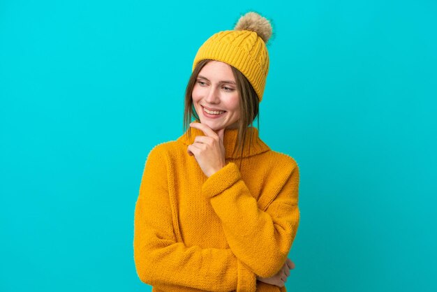 Giovane donna inglese che indossa una giacca invernale isolata su sfondo blu che guarda al lato