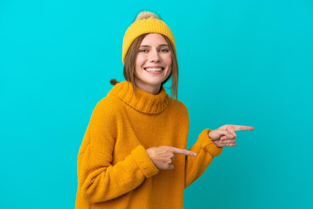 Giovane donna inglese che indossa una giacca invernale isolata su sfondo blu sorpreso e indicando il lato