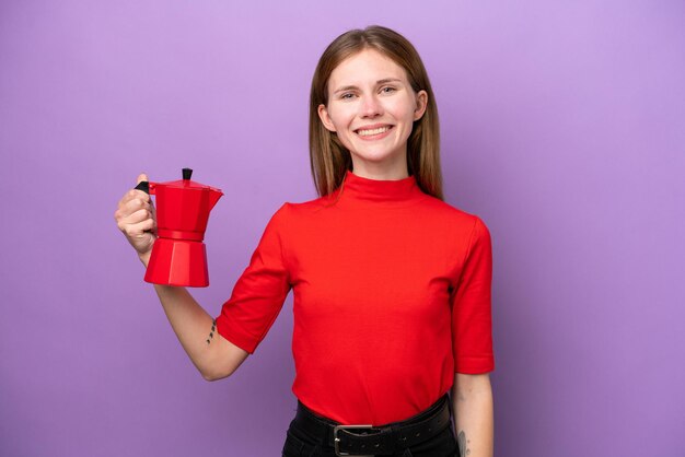 Giovane donna inglese che tiene caffettiera isolata su sfondo viola che sorride molto