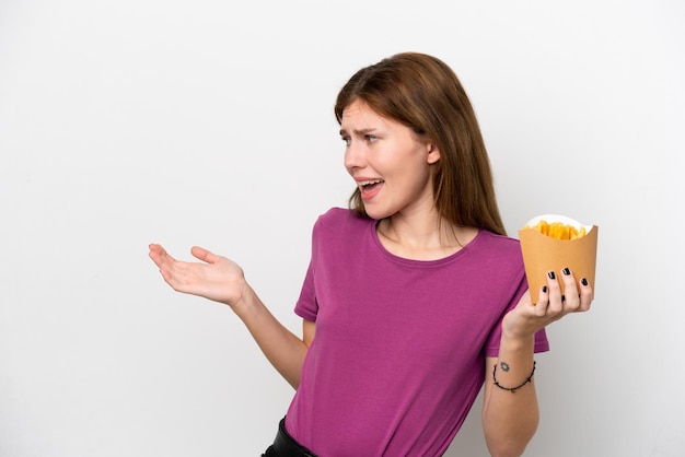 Giovane donna inglese che tiene patatine fritte isolate su sfondo bianco con espressione a sorpresa mentre guarda di lato