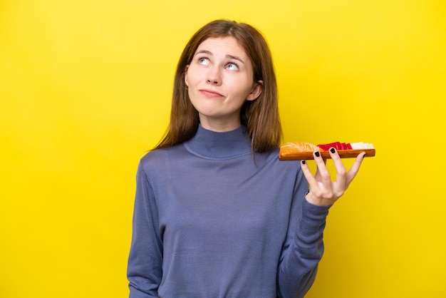 Giovane donna inglese che tiene sashimi isolato su sfondo giallo e alzando lo sguardo